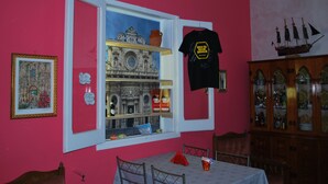 A room with a pink wall, a window with a view of a historical building, a black t-shirt hanging, and a ship model. - A casa di Mich il Salento Lu sule Lu mare Lu ientu (Monteroni di Lecce)