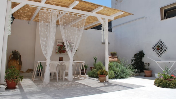 A covered patio area with a white table and chairs, surrounded by potted plants and a pergola with a white canopy. - A casa di Mich il Salento Lu sule Lu mare Lu ientu (Monteroni di Lecce)