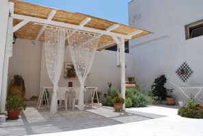 A covered patio area with a white table and chairs, surrounded by potted plants and a pergola with a white canopy. - A casa di Mich il Salento Lu sule Lu mare Lu ientu (Monteroni di Lecce)