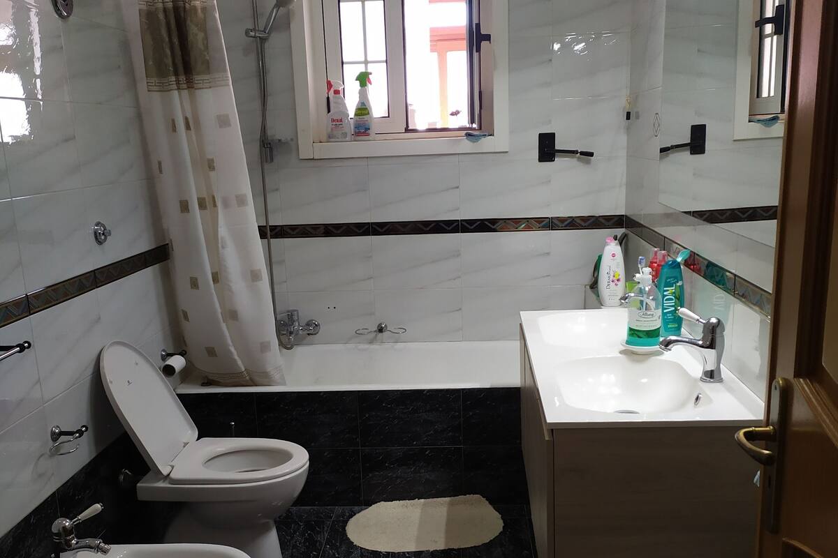 A bathroom with a toilet, bidet, and sink. There is a window with a view of the outside.