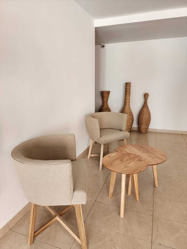 A modern living room with a round wooden coffee table, two beige armchairs, and two wicker vases on the wall.
