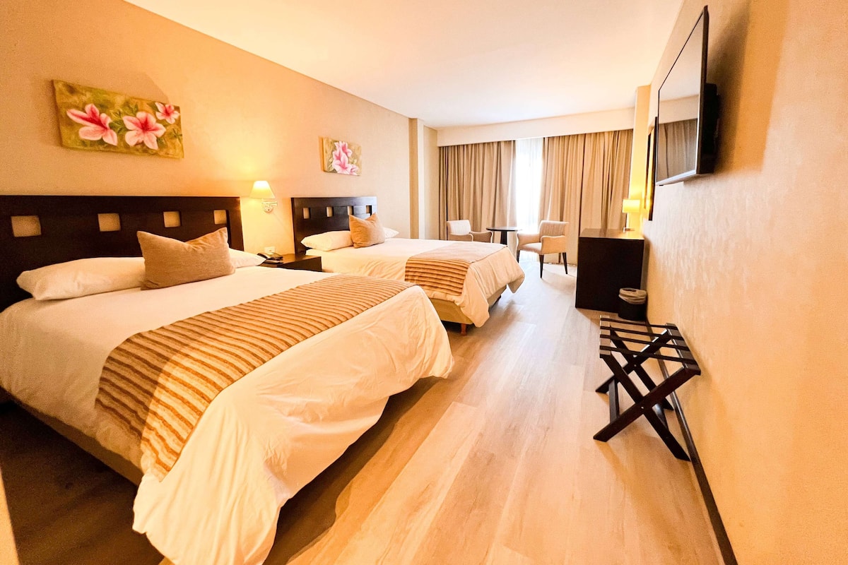 A hotel room with two beds, a TV, a desk, and a chair.