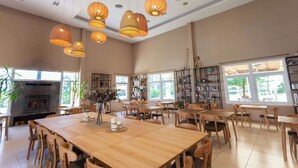 A spacious room with a large wooden table, multiple chairs, hanging pendant lights, a fireplace, and large windows providing natural light. - Howard Johnson by Wyndham Funes (Funes)