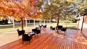 An outdoor wooden deck with tables and chairs, surrounded by trees with autumn foliage. - Howard Johnson by Wyndham Funes (Funes)