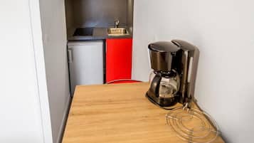 A small kitchenette with a microwave, sink, and red cabinets. There is a wooden table with a coffee maker and a red chair.
