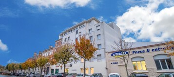 Un immeuble à plusieurs étages, avec une enseigne indiquant « Pneus & Cie » au rez-de-chaussée.