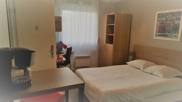 Une chambre d’hôtel comprenant un lit, un bureau avec une chaise, une armoire et une machine à café.