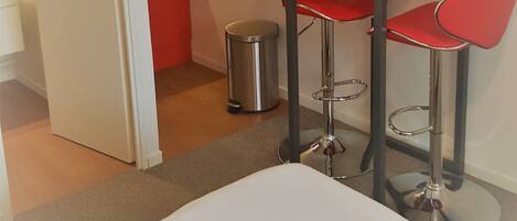 Une chambre d’hôtel avec un lit, une petite kitchenette et deux tabourets de bar rouges.
