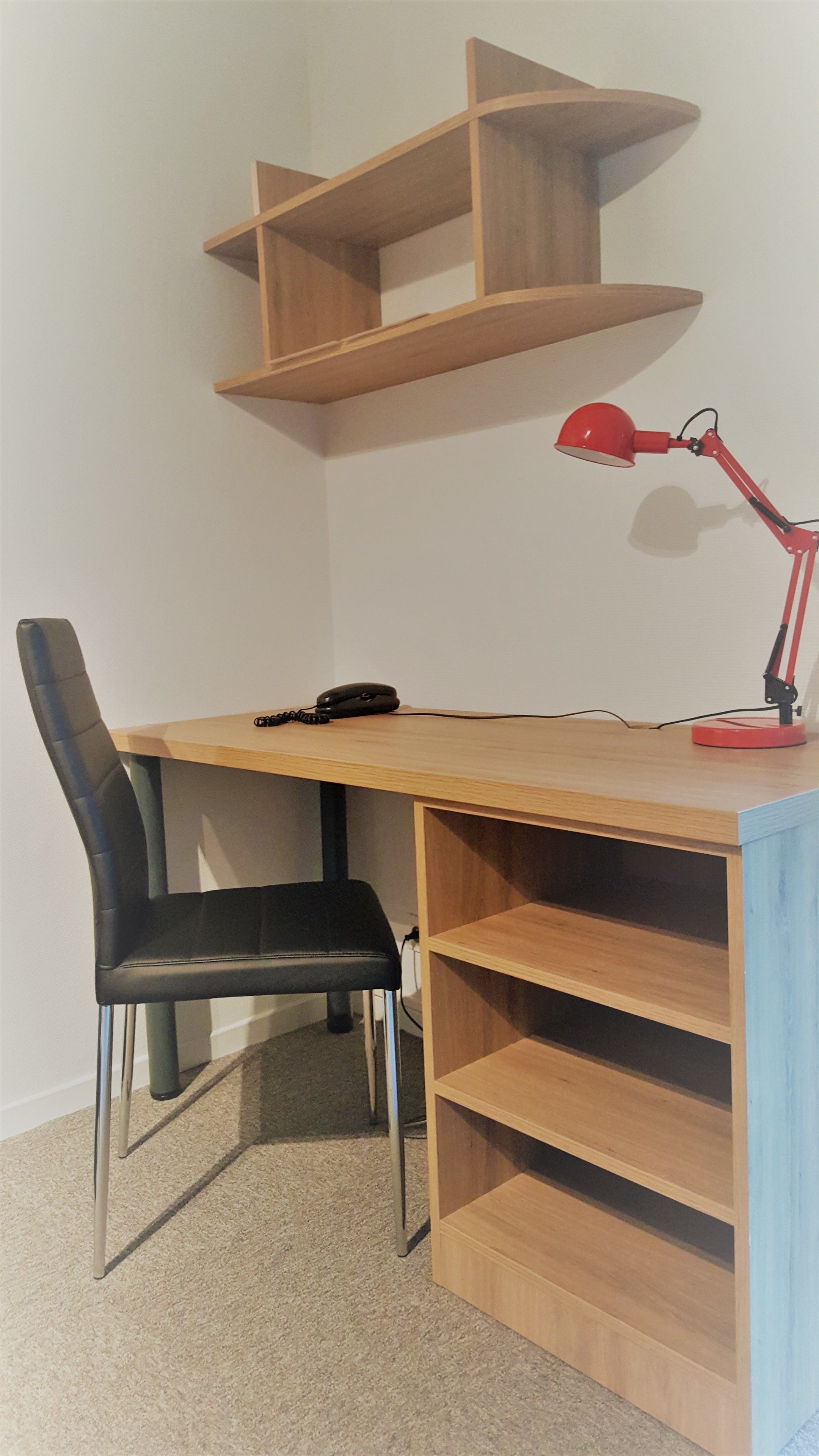 A corner desk with a black chair, a red desk lamp, and a telephone.