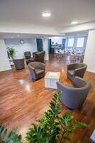 Un vaste espace salon doté d’un plancher en bois, de plusieurs fauteuils gris, d’une table basse et, au fond, d’un coin repas.