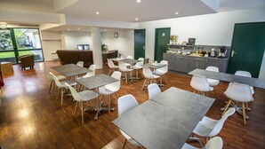 Een moderne eetruimte met meerdere tafels en stoelen, een keuken met apparatuur, en uitzicht op de omgeving.