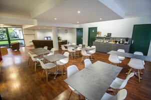Un espace repas moderne avec plusieurs tables et chaises, un coin cuisine équipé d’appareils électroménagers et une vue sur l’extérieur.