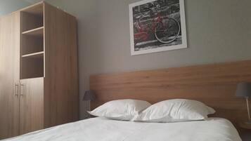 A hotel room with a wooden headboard, a bed with white linens, a large wardrobe, and a framed picture of a bicycle on the wall.
