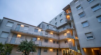 Un immeuble résidentiel à plusieurs étages, doté de balcons, d’une cour intérieure et d’un éclairage extérieur.