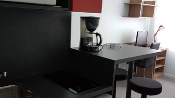 Cocina compacta con microondas, cafetera y refrigerador. Incluye un lavamanos pequeño y un taburete de bar.
