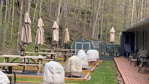 A covered outdoor seating area with picnic tables and umbrellas, surrounded by a forest. - Starlite Motel (Big Indian)
