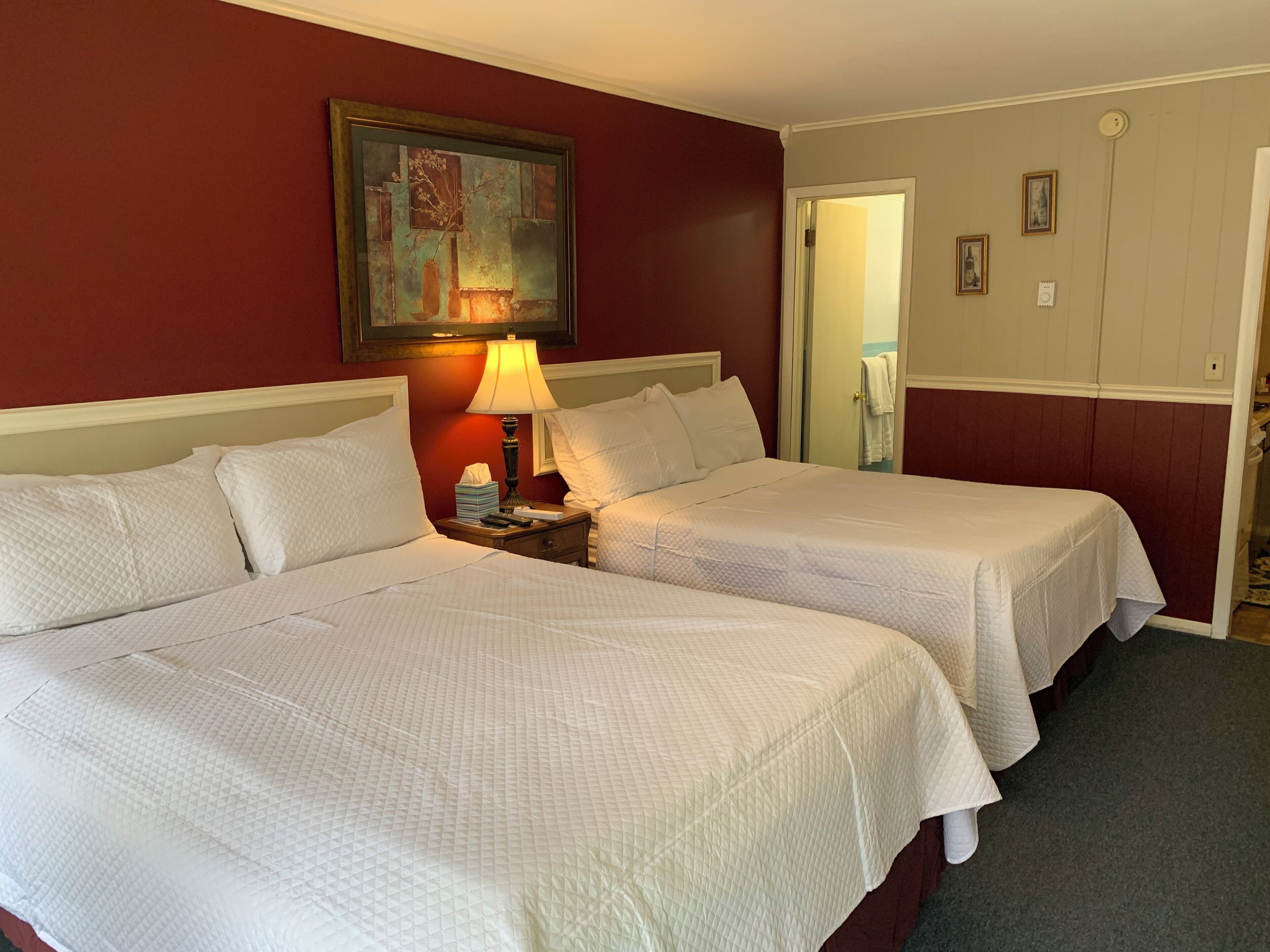 A hotel room with two beds, a nightstand with a lamp, and a painting on the wall.