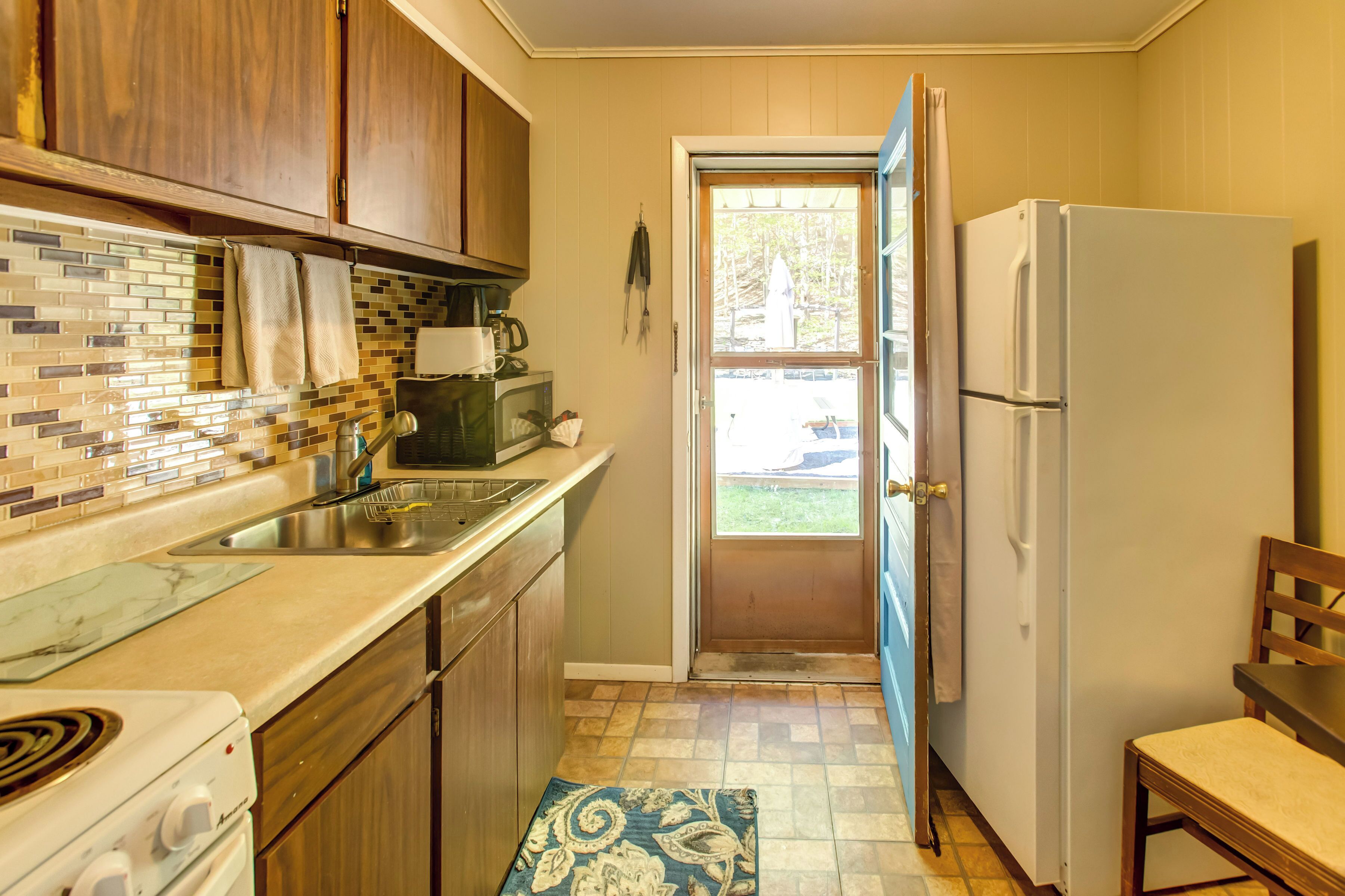 A kitchen with wooden cabinets, a tiled backsplash, a white refrigerator, and a door leading to a patio.