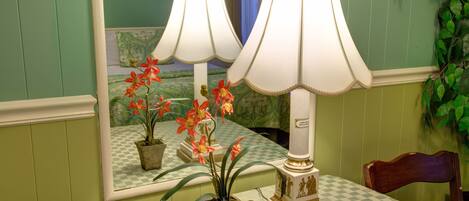 Una habitación con mantel a cuadros, una lámpara y un espejo que refleja una cama y una ventana con cortinas.