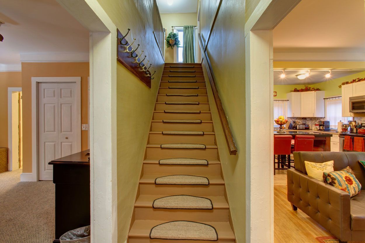 A staircase with a handrail and carpeted steps leading to a kitchen area with a microwave and bar stools.