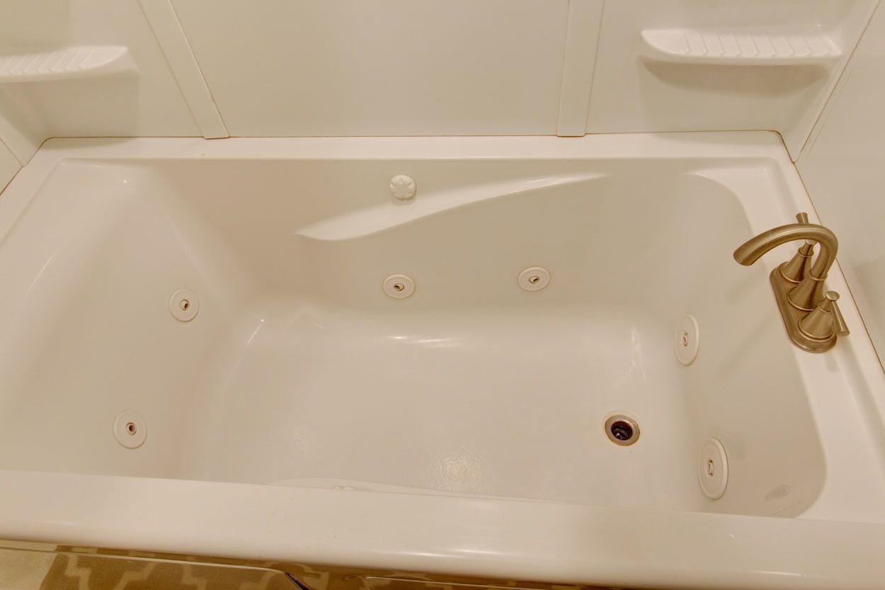 A white bathtub with a single gold faucet, four drain holes, and a single plug.