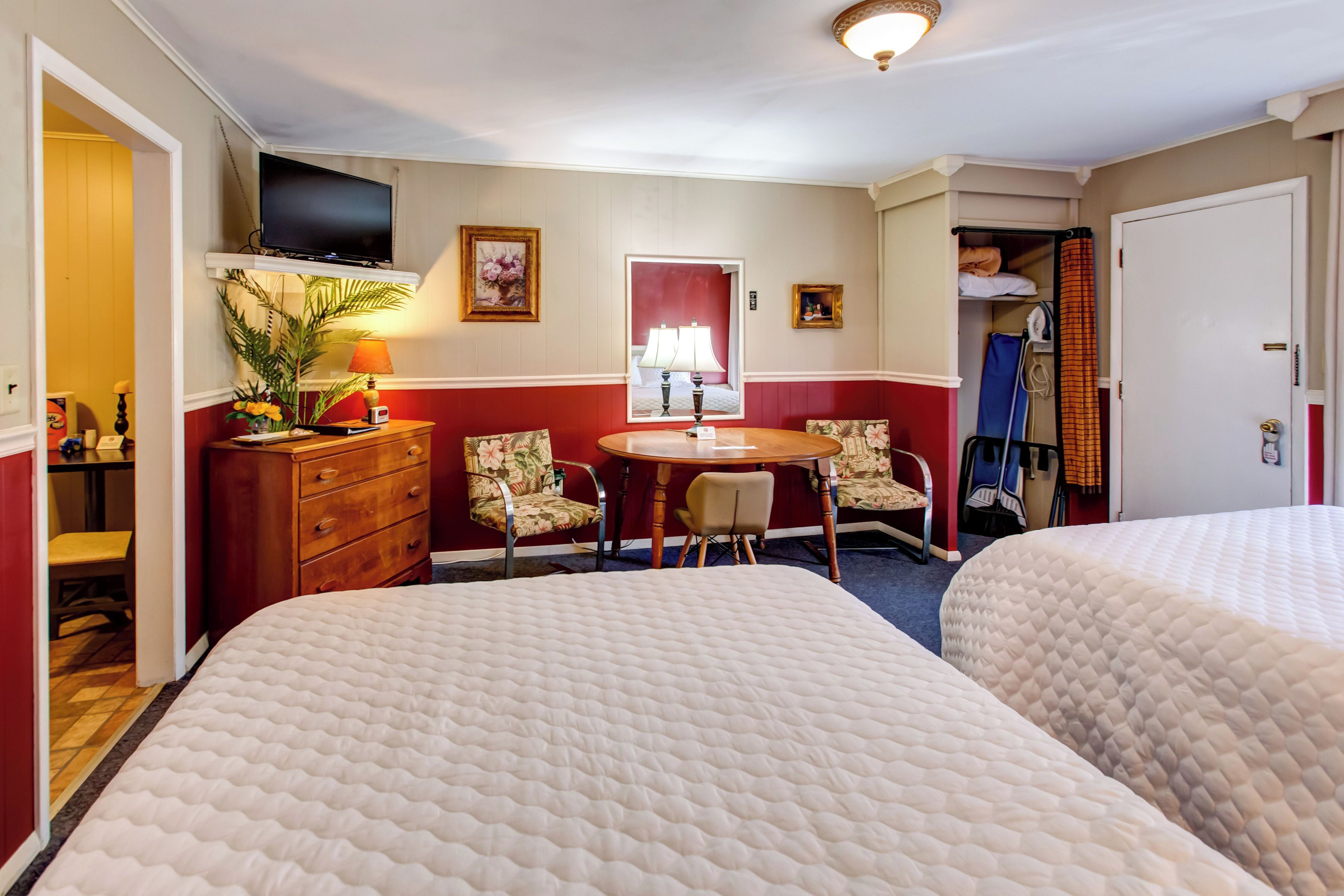 A hotel room with two beds, a TV, a dining table with chairs, a desk, and a wardrobe.