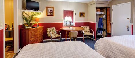 A hotel room with two beds, a TV, a dining table with chairs, a desk, and a wardrobe.