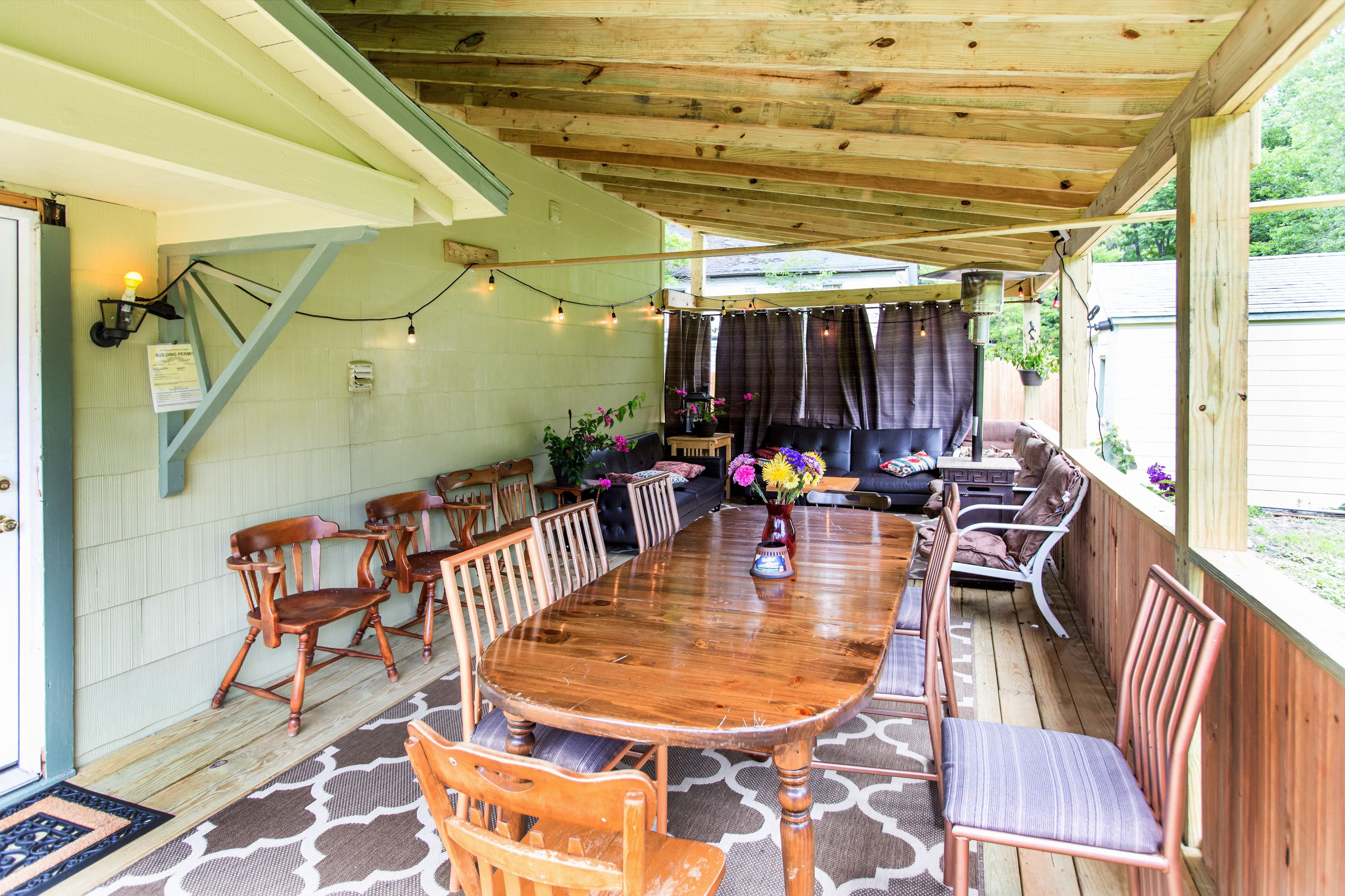 Un patio cubierto con una mesa y sillas de madera, un sofá y un pequeño jardín con plantas en macetas.