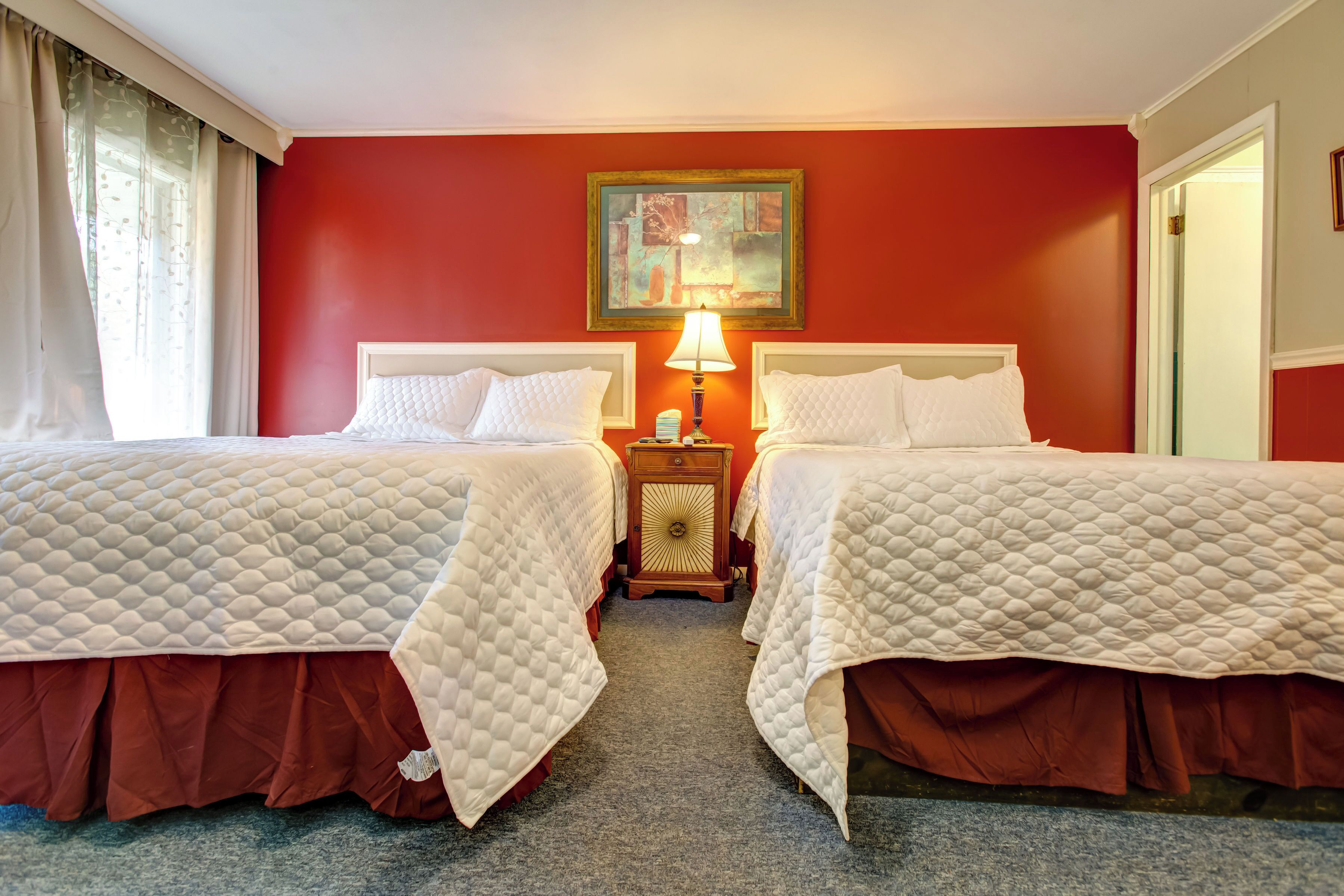 Habitación de hotel con dos camas, una mesita de noche con lámpara y un cuadro en la pared.