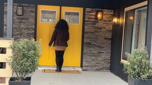 A person walking towards a yellow door with stone walls and a bench to the left. - Starlite Motel (Big Indian)