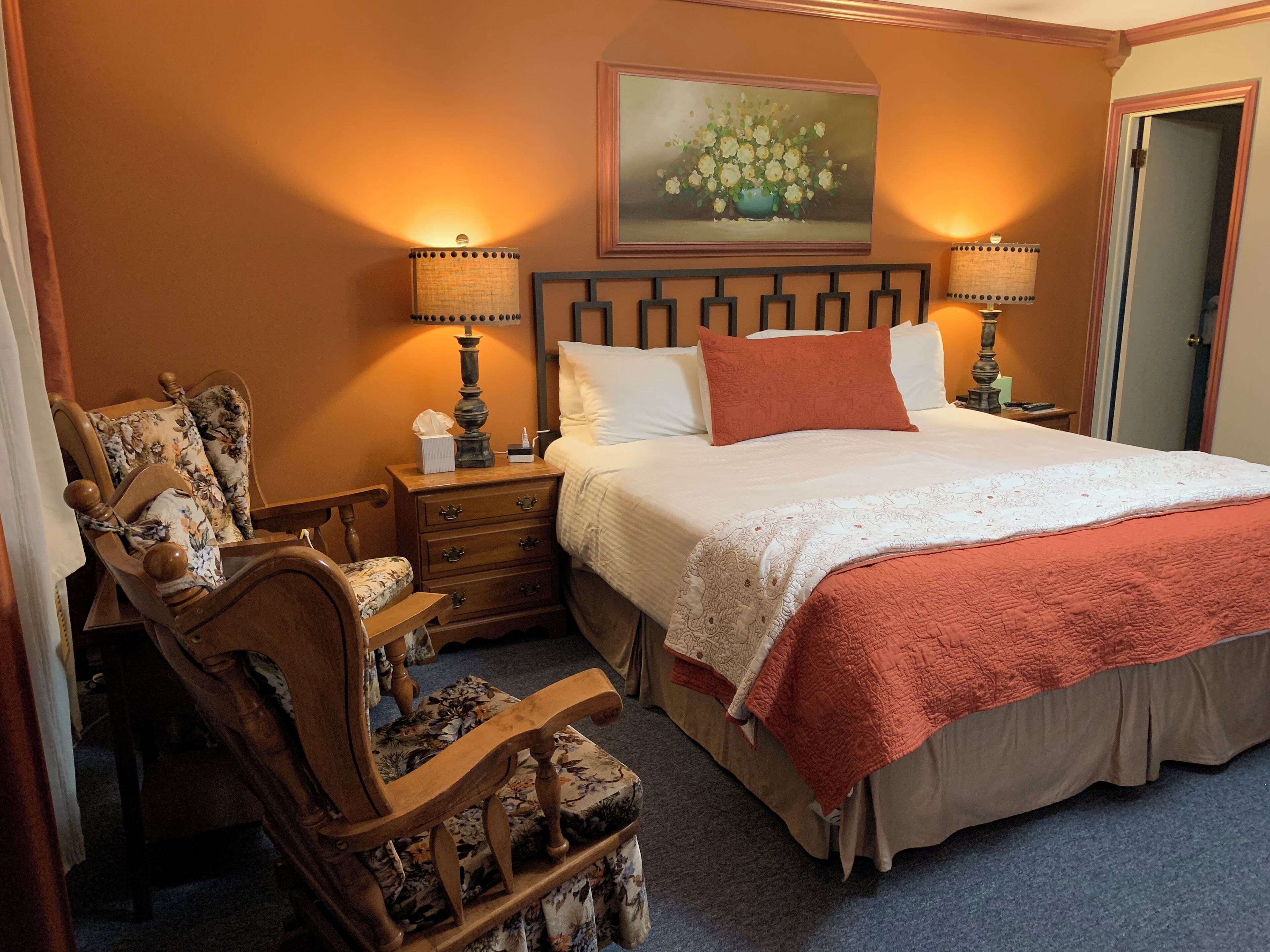 Une chambre à coucher bien rangée, avec un grand lit, deux tables de chevet avec des lampes, une chaise et un tableau au mur.
