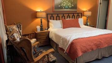 Une chambre à coucher bien rangée, avec un grand lit, deux tables de chevet avec des lampes, une chaise et un tableau au mur.