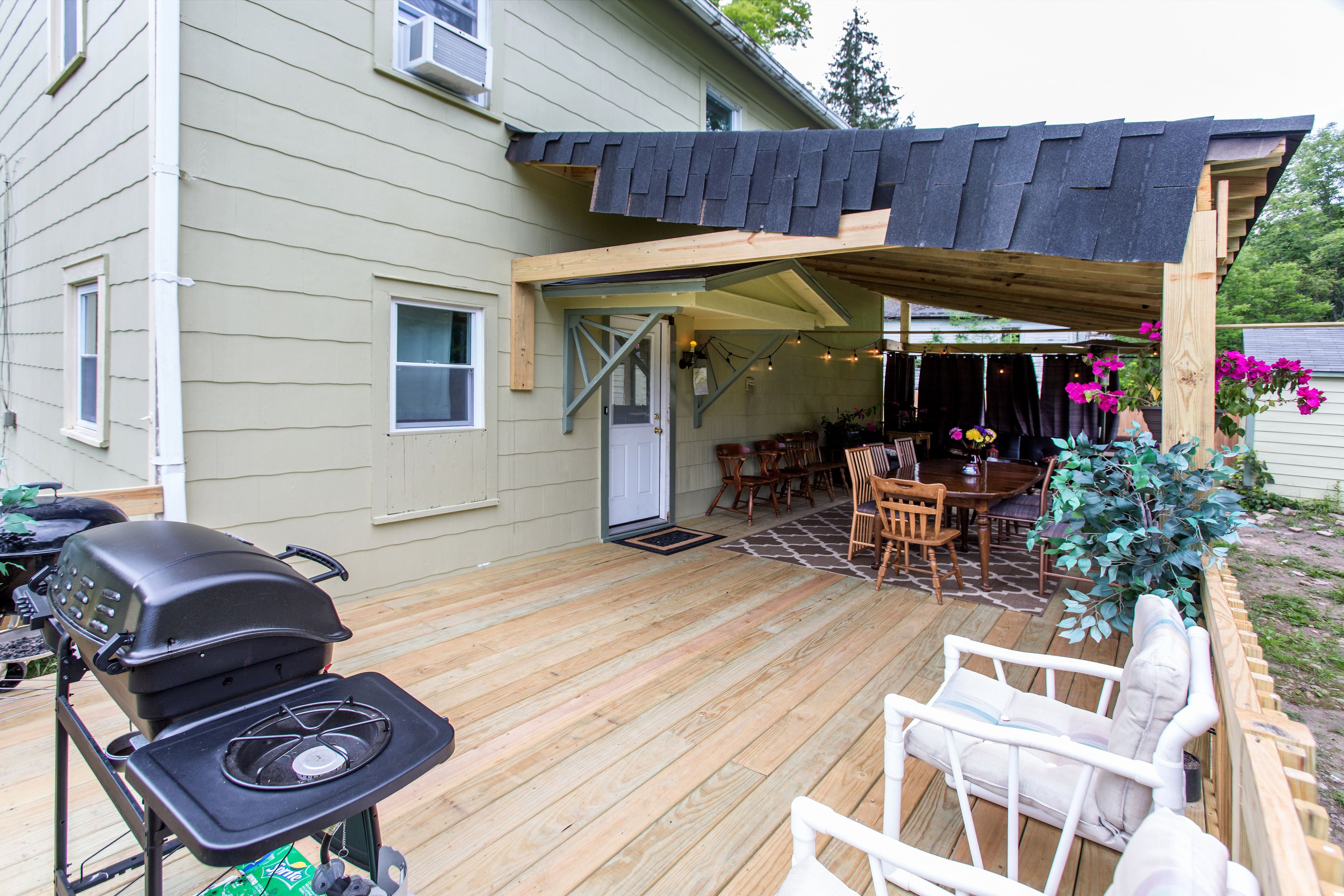 A covered outdoor patio with a grill, seating area, and a wooden deck.
