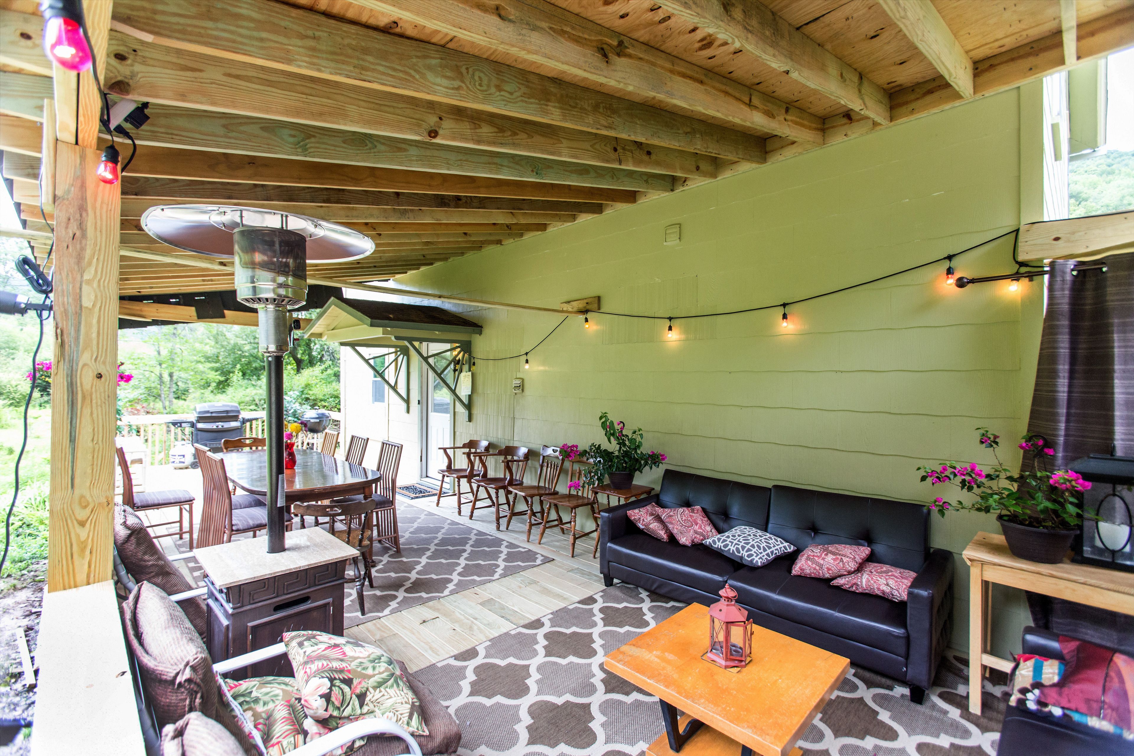 Un espace de vie extérieur abrité, doté d’un plafond en bois, d’un canapé en cuir noir, d’une table à manger avec des chaises et d’un barbecue.