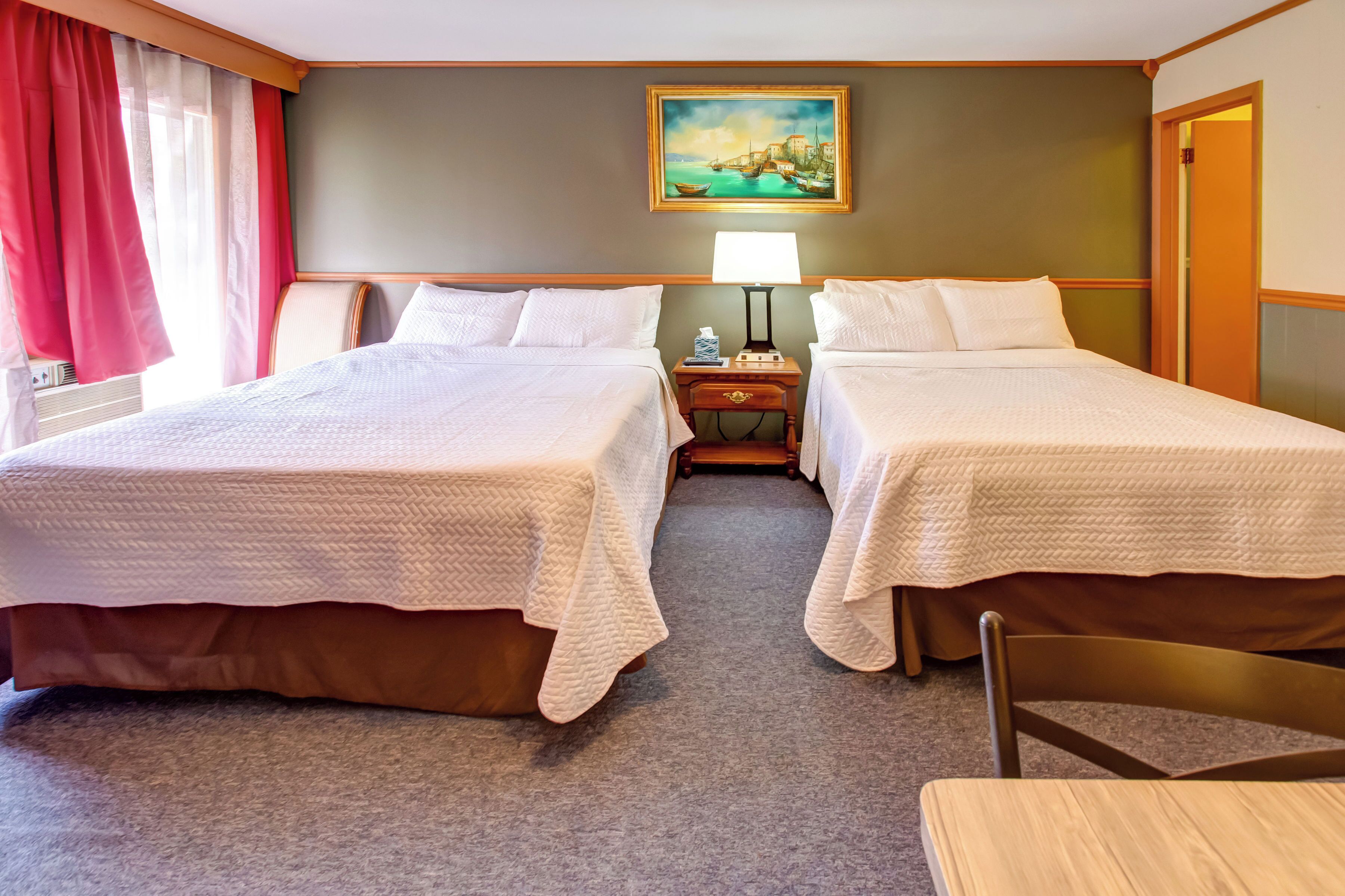 Una habitación de hotel con dos camas, una mesita de noche, una lámpara y un cuadro en la pared.