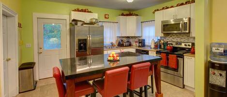 Una cocina con isla central, armarios blancos, electrodomésticos de acero inoxidable y taburetes rojos.