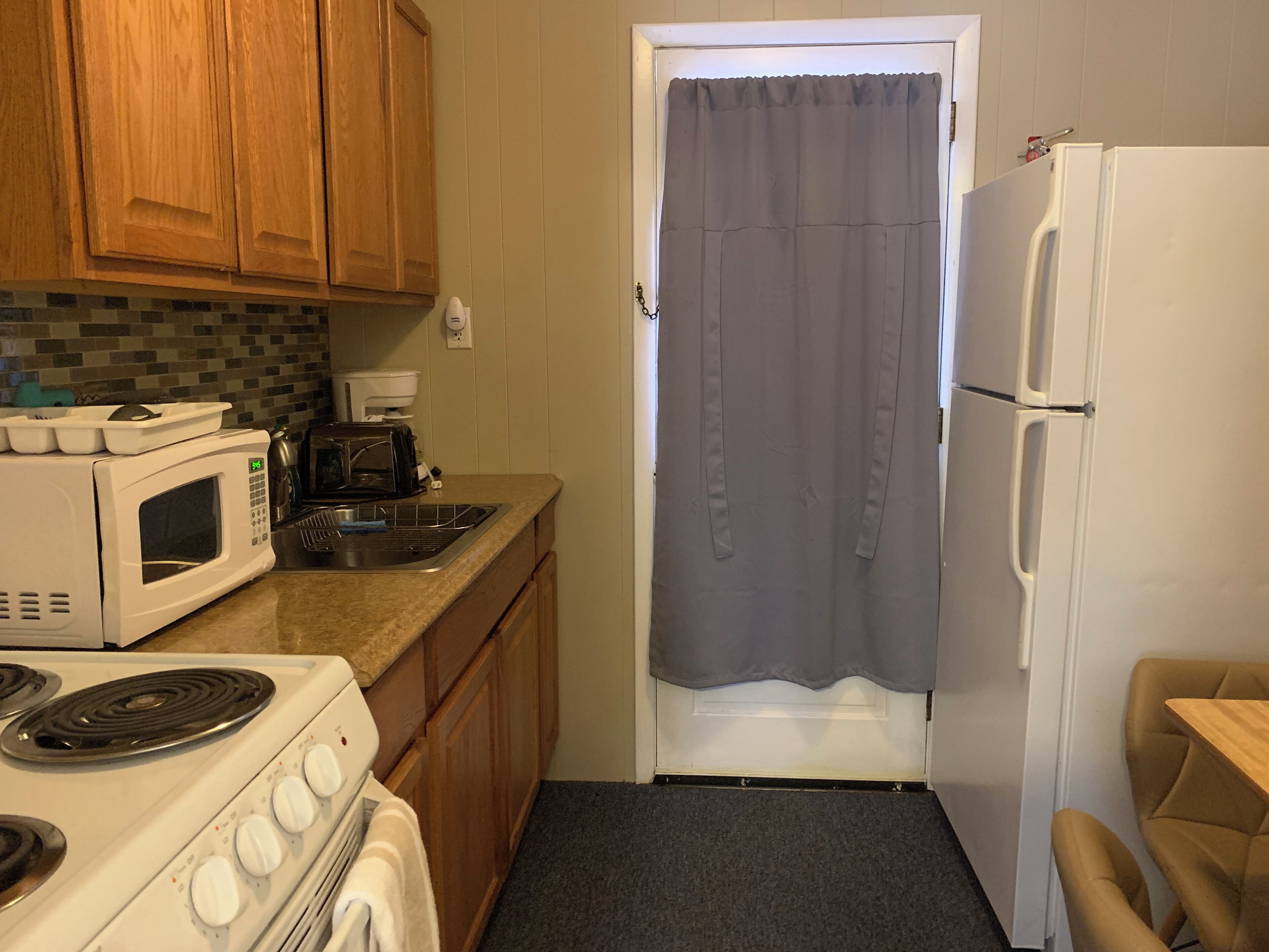 A compact kitchen with wooden cabinets, a microwave, a stove, a refrigerator, and a small sink.