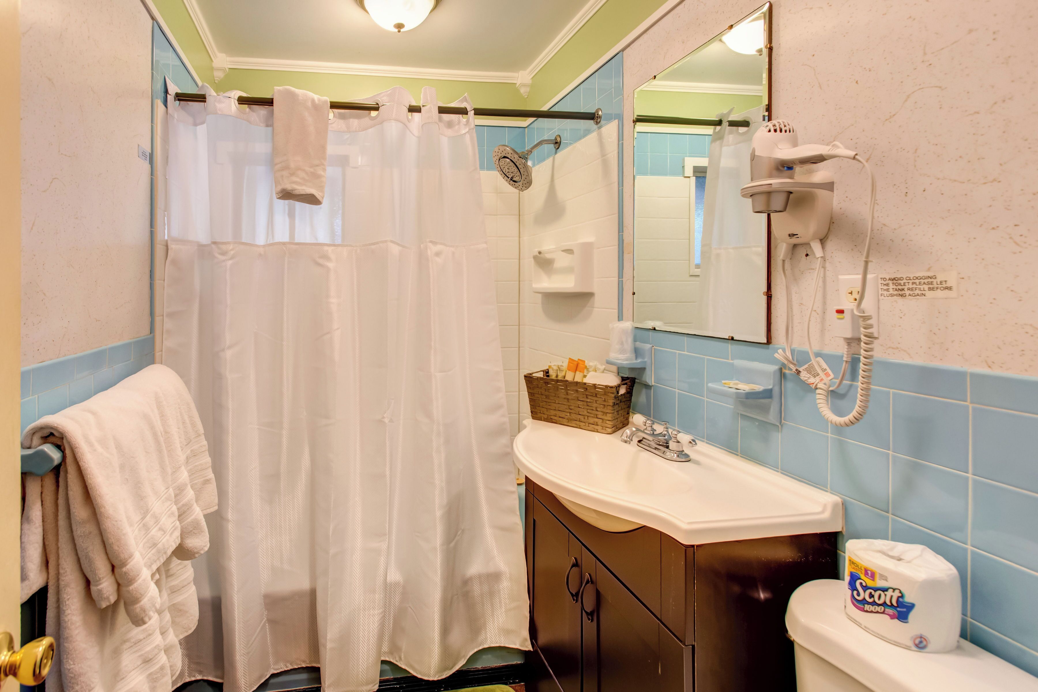 A bathroom with a shower curtain, a sink, a toilet, and a hairdryer mounted on the wall.