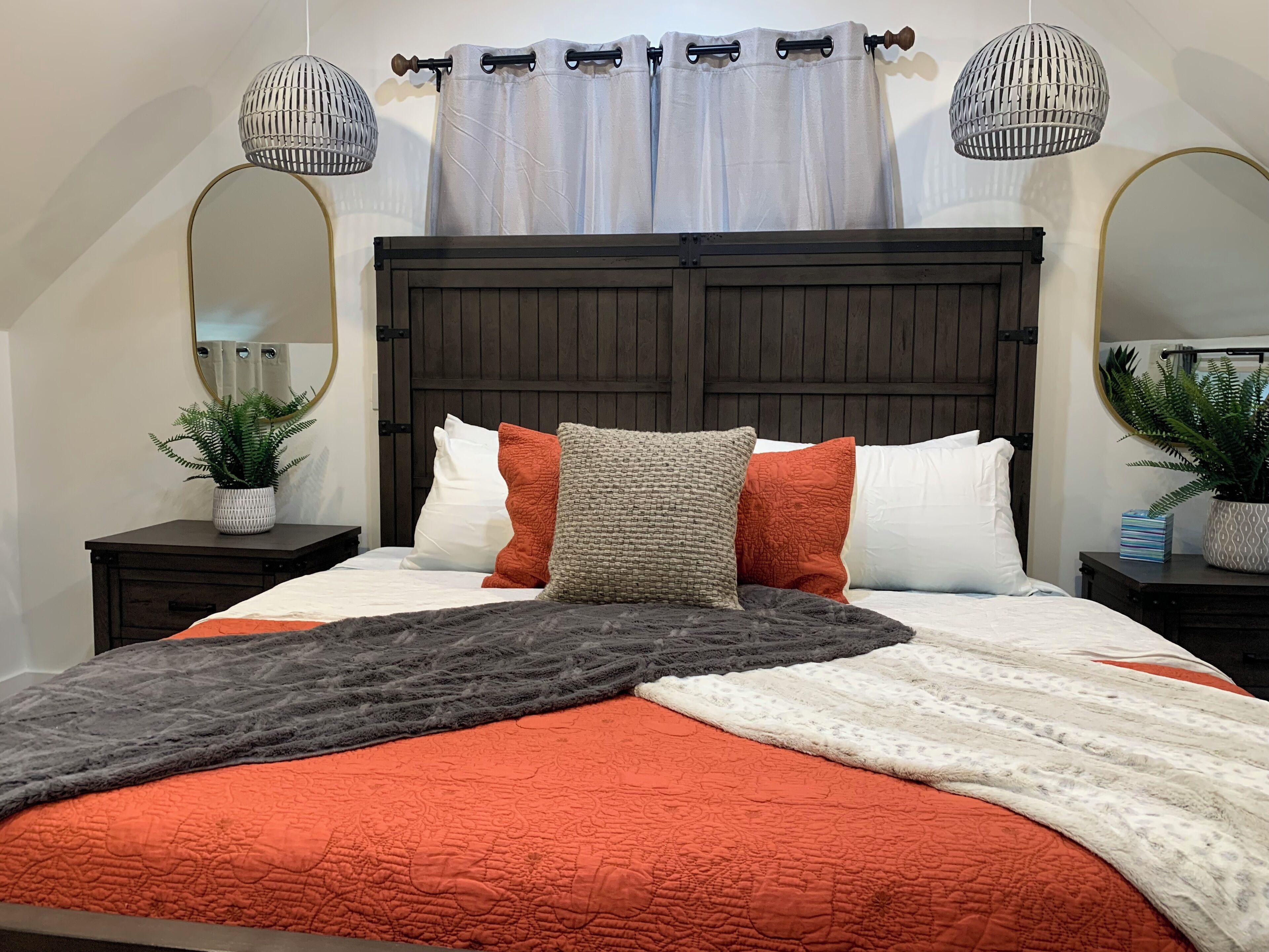 A bedroom with a large bed, dark wooden headboard, two bedside tables with plants, and a ceiling light fixture.