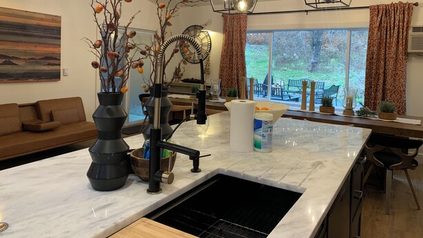 A modern kitchen with a central island, a dining area with a sofa, and a large window with a view of the outdoors. - Starlite Motel (Big Indian)