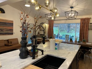 A modern kitchen with a central island, a dining area with a sofa, and a large window with a view of the outdoors. - Starlite Motel (Big Indian)