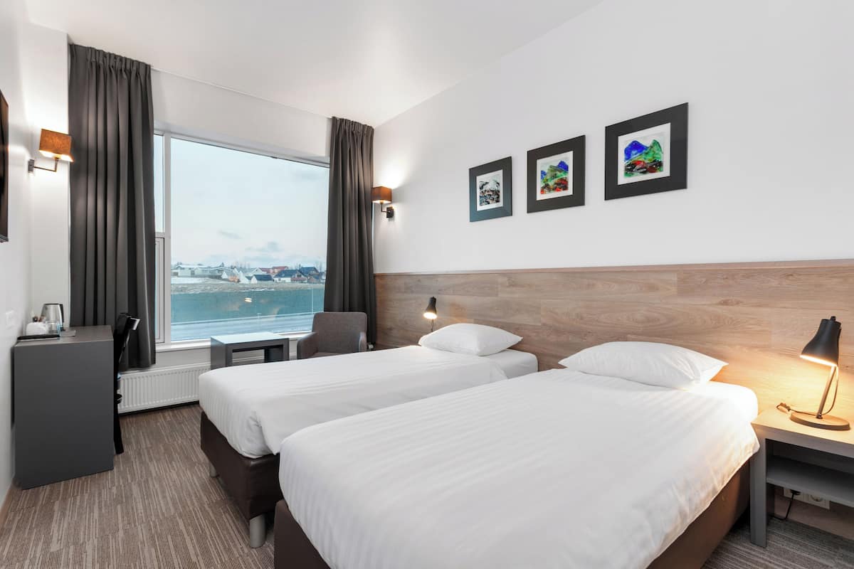 Une chambre d’hôtel avec deux lits, un bureau, une chaise, une fenêtre donnant sur la mer et trois tableaux encadrés accrochés au mur.