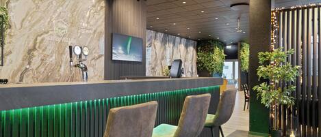 A modern reception area with a marble wall, a mounted television, and a bar counter with green lighting.