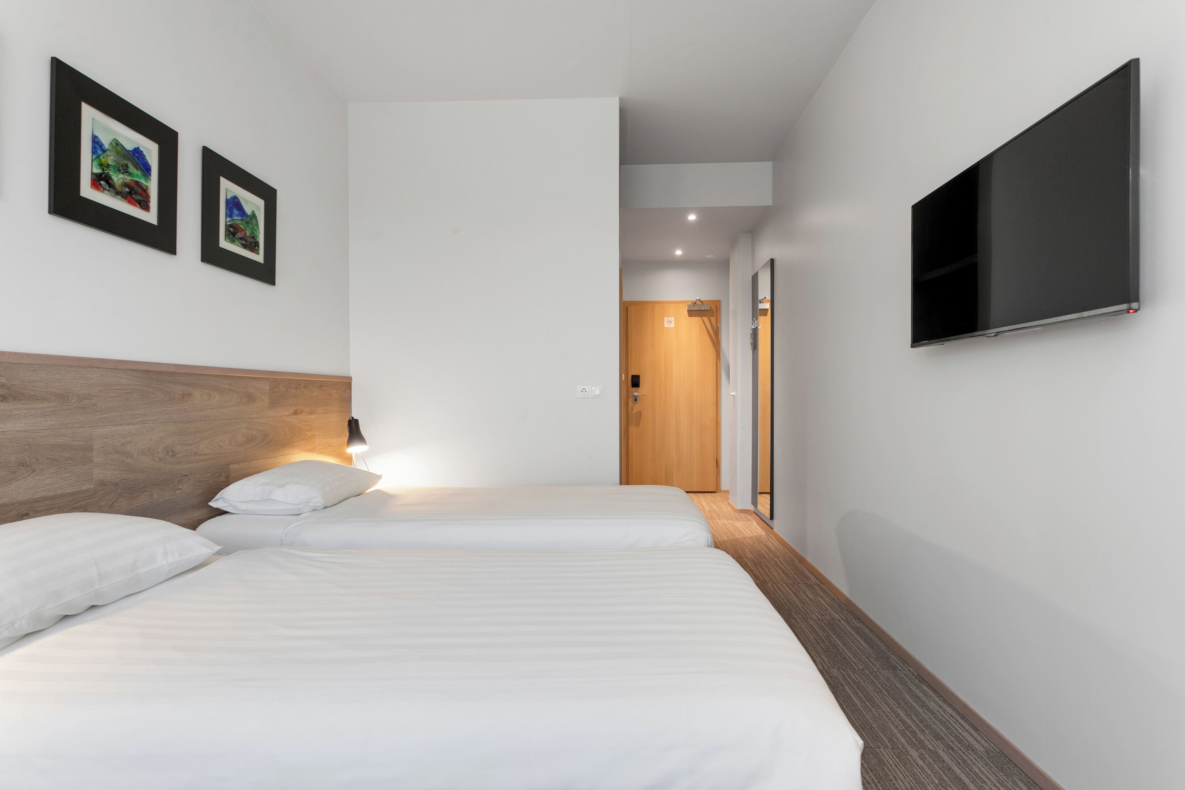 A hotel room with two beds, a TV mounted on the wall, and two framed pictures on the wall.