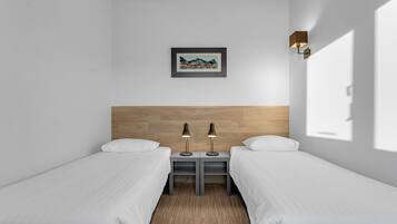 Une chambre d’hôtel avec deux lits simples, une tête de lit en bois, un tableau encadré et deux lampes de chevet.