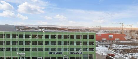 Un hotel verde con restaurante y gimnasio, que destaca por su diseño moderno, amplias ventanas y techo plano.