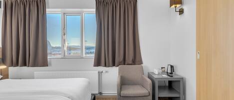 Hotellihuone, jossa on sänky, tuoli, pieni pöytä ja vedenkeitin sekä ikkunasta avautuva näkymä kaupungin ylle.