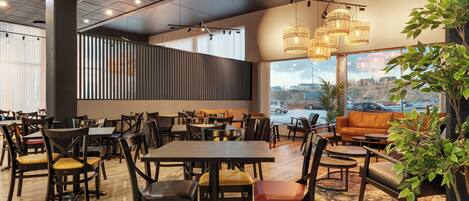 Un restaurante espacioso con varias mesas y sillas, amplias ventanas que ofrecen vistas de la ciudad y una zona de estar acogedora con un sofá y plantas.