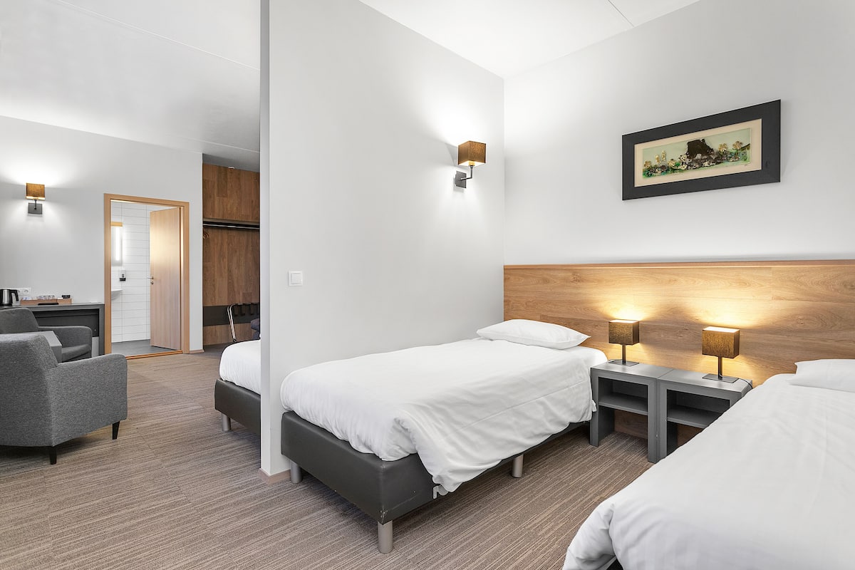 Une chambre d’hôtel avec deux lits simples, un bureau, une chaise et une tête de lit en bois.
