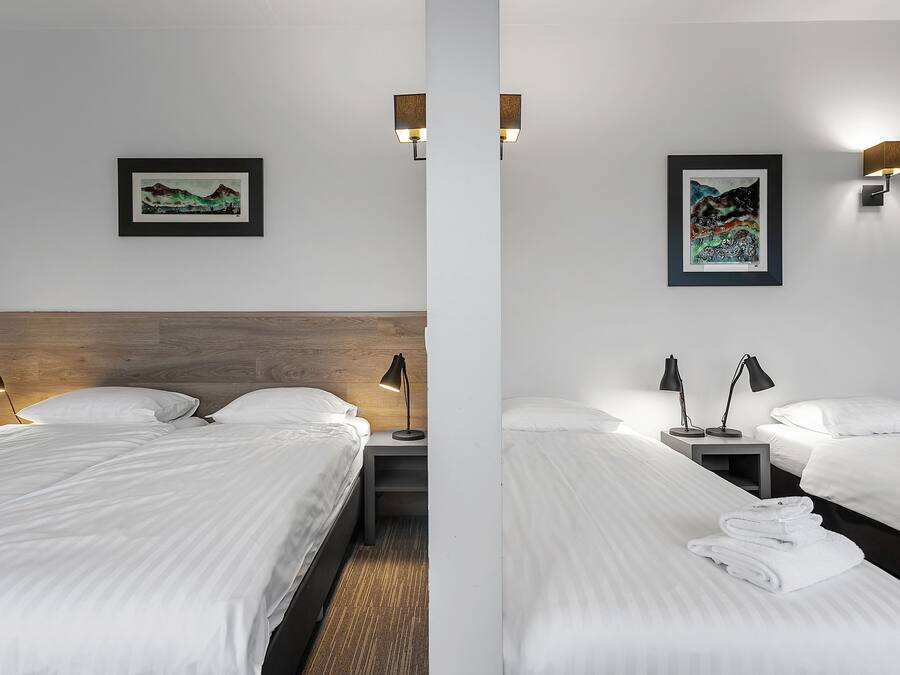 A hotel room with two beds, a wooden headboard, a nightstand with a lamp, and two wall-mounted lamps.